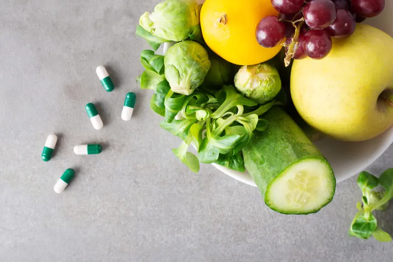 Bol de gros plan avec des fruits et légumes et des pilules Adeline Collet docteure en pharmacie et diététicienne nutritionniste à Bordeaux